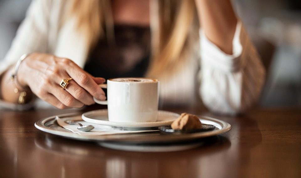 Woman enjoying a cappuccino at a cafe table.
