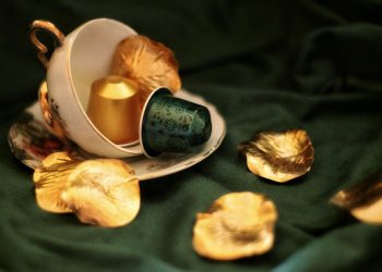 Tea cup with coffee pods and golden leaves on green fabric.