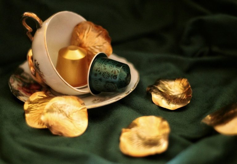Tea cup with coffee pods and golden leaves on green fabric.