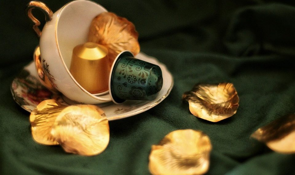 Tea cup with coffee pods and golden leaves on green fabric.