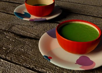 Two vibrant red bowls of matcha tea on artistic saucers on wooden table.