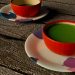 Two vibrant red bowls of matcha tea on artistic saucers on wooden table.