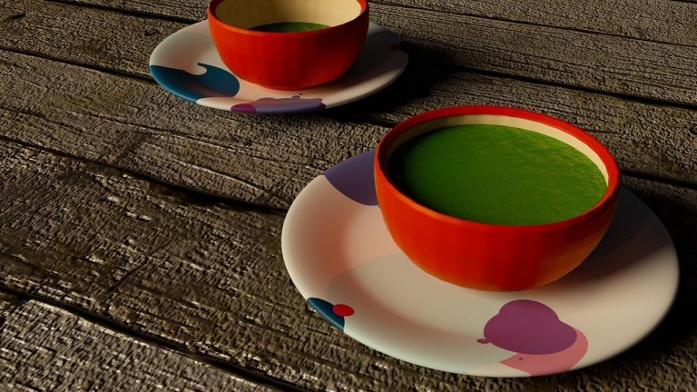Two vibrant red bowls of matcha tea on artistic saucers on wooden table.