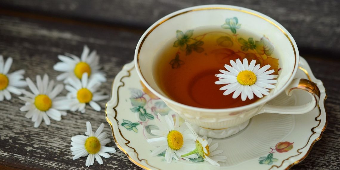 Tea cup with chamomile flowers on wooden table.