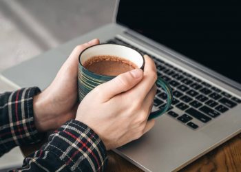 Hands holding a coffee mug near a laptop.