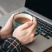 Hands holding a coffee mug near a laptop.