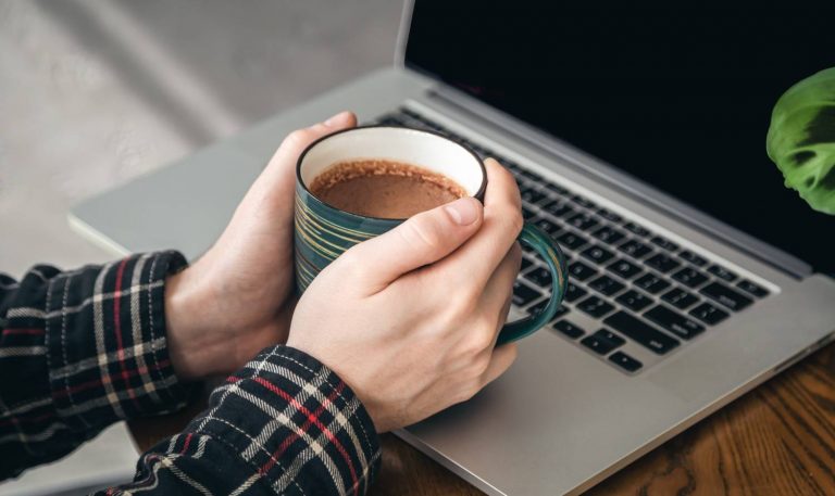Hands holding a coffee mug near a laptop.