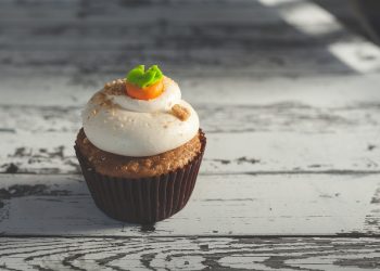 Carrot cupcake topped with frosting on rustic table.