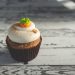Carrot cupcake topped with frosting on rustic table.