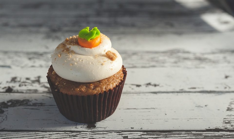 Carrot cupcake topped with frosting on rustic table.