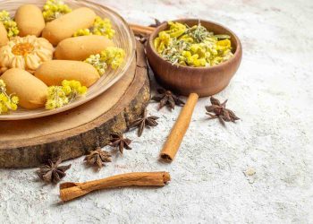 Plate of cookies with flowers, star anise, and cinnamon sticks on rustic surface.