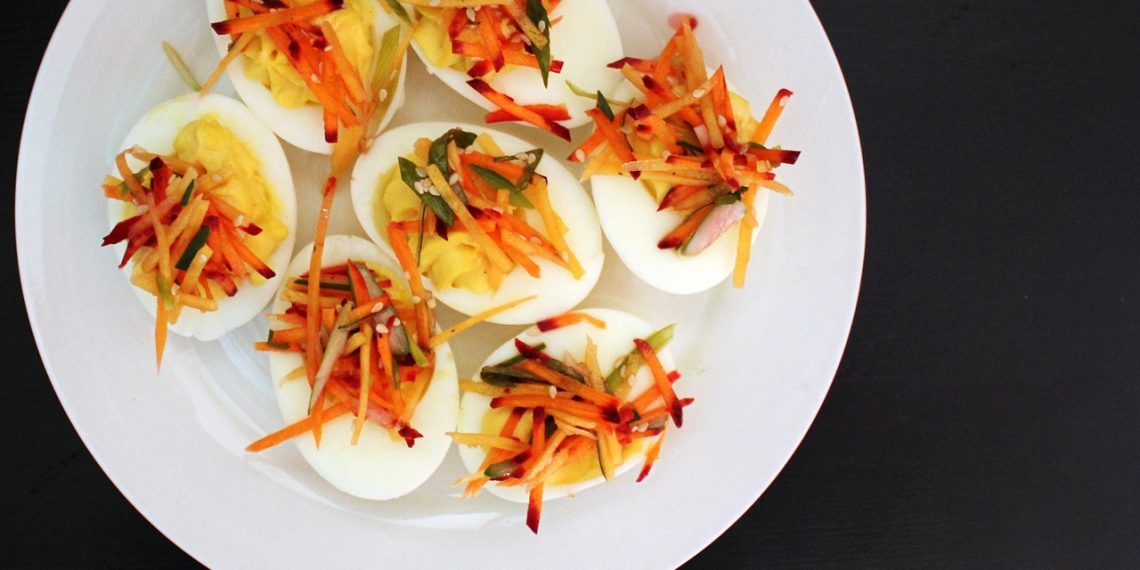 Deviled eggs topped with shredded vegetables on white plate.