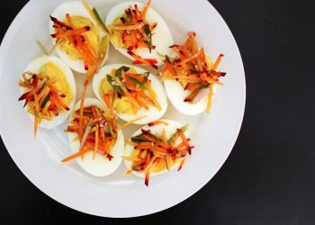 Deviled eggs topped with shredded vegetables on white plate.