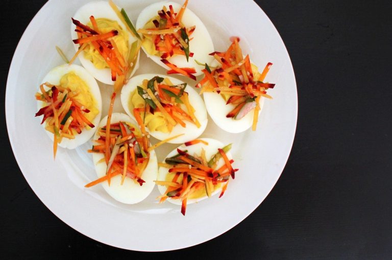 Deviled eggs topped with shredded vegetables on white plate.