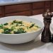Bowl of pasta with kale next to pepper grinders on a kitchen counter.