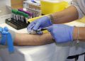 Nurse drawing blood with syringe for lab testing.