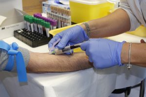 Nurse drawing blood with syringe for lab testing.