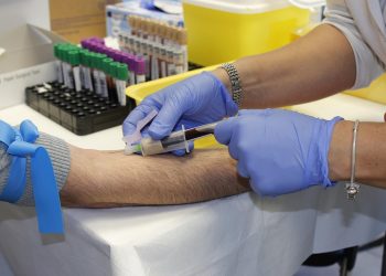 Nurse drawing blood with syringe for lab testing.
