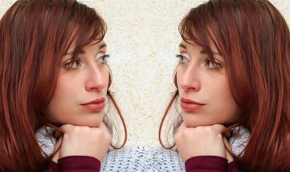 Two women with red hair wearing sweaters face each other.