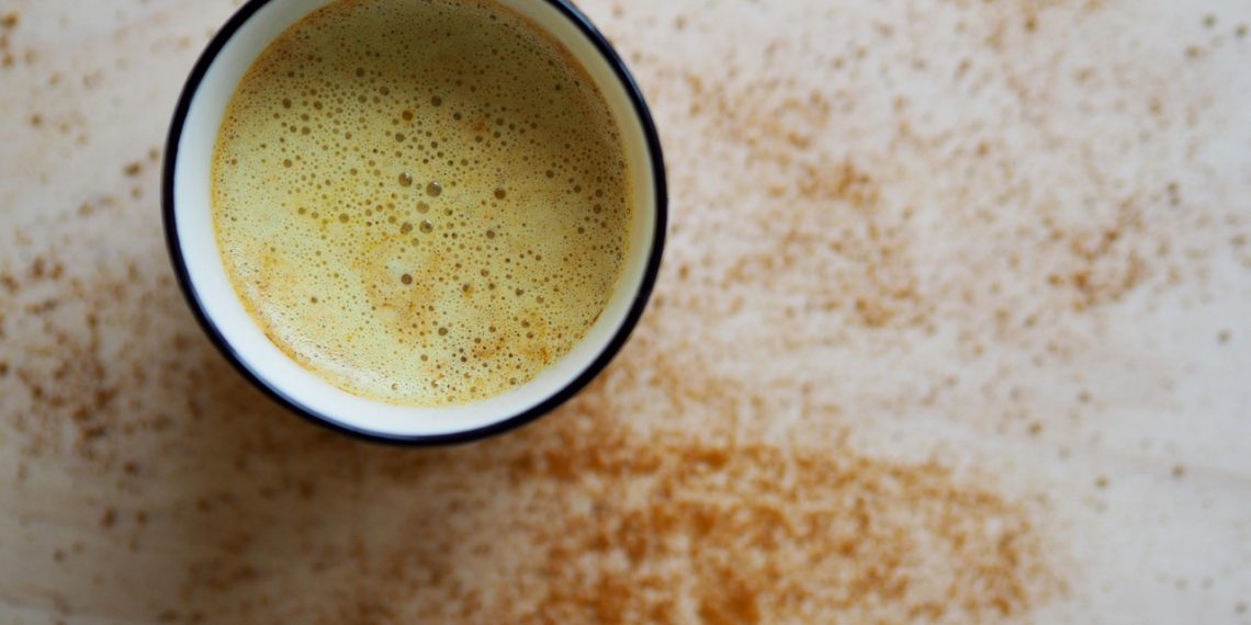 Creamy turmeric latte with cinnamon sprinkle on a light surface.