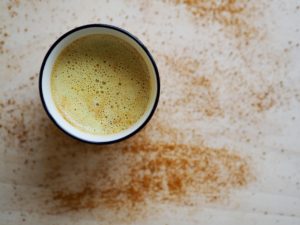 Creamy turmeric latte with cinnamon sprinkle on a light surface.