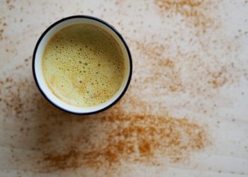 Creamy turmeric latte with cinnamon sprinkle on a light surface.