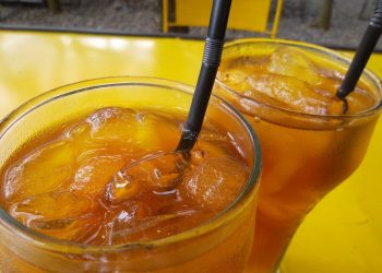 Two glasses of iced tea on a yellow table.
