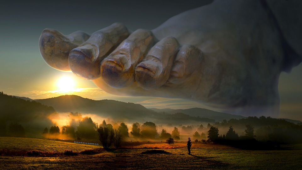 Giant stone foot hovering over misty landscape at sunrise.