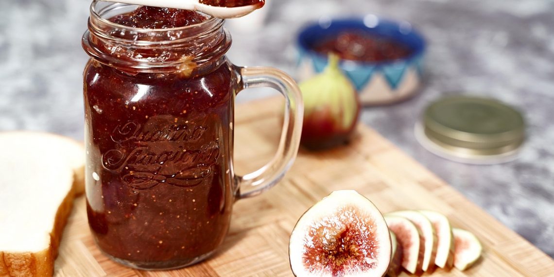 Homemade fig jam in a jar with fresh figs and sliced bread.