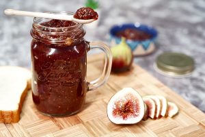Homemade fig jam in a jar with fresh figs and sliced bread.