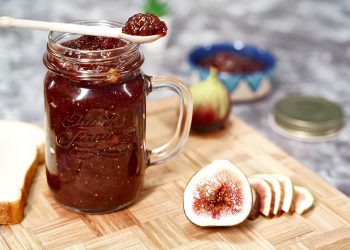 Homemade fig jam in a jar with fresh figs and sliced bread.