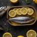 Fresh fish garnished with lemon slices in a tray, surrounded by whole lemons.