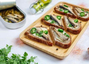 Toasted rye bread with sardines, jalapeño, and fresh coriander on a wooden tray.