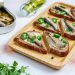 Toasted rye bread with sardines, jalapeño, and fresh coriander on a wooden tray.