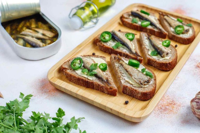 Toasted rye bread with sardines, jalapeño, and fresh coriander on a wooden tray.