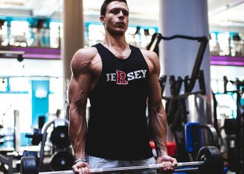 Man lifting weights in gym in Jersey tank top.