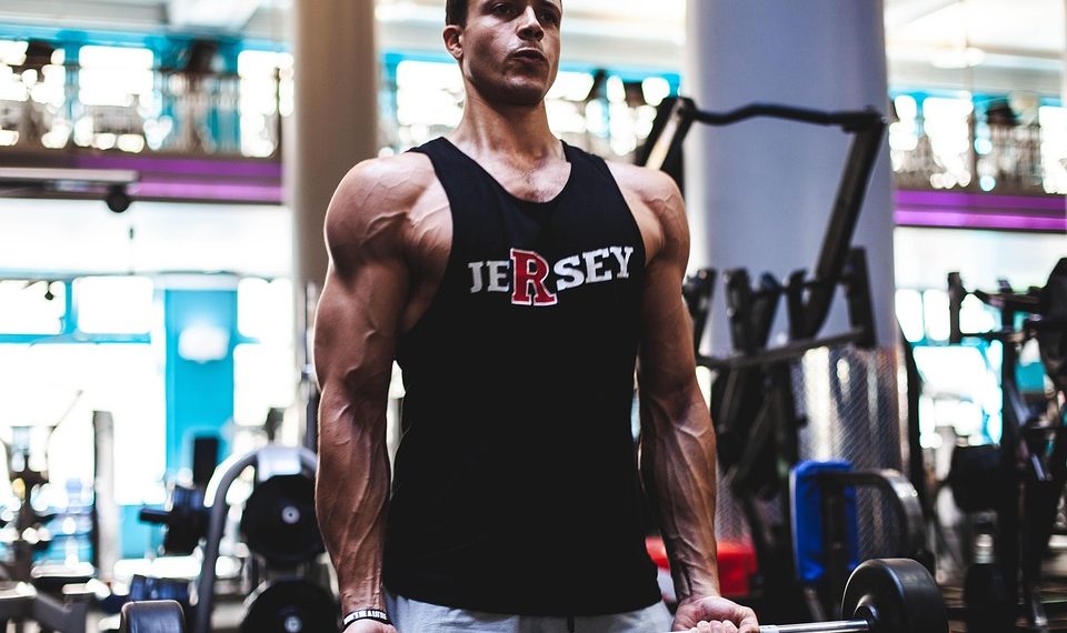 Man lifting weights in gym in Jersey tank top.