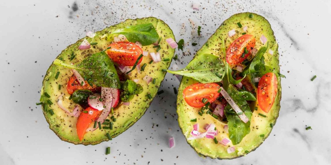 Avocado halves topped with cherry tomatoes, onions, and fresh greens.
