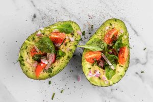 Avocado halves topped with cherry tomatoes, onions, and fresh greens.