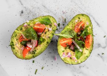 Avocado halves topped with cherry tomatoes, onions, and fresh greens.