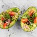 Avocado halves topped with cherry tomatoes, onions, and fresh greens.