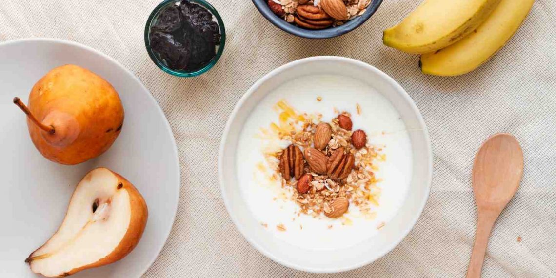 yogurt with almonds and granola, surrounded by pears, bananas, and prunes