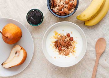 yogurt with almonds and granola, surrounded by pears, bananas, and prunes