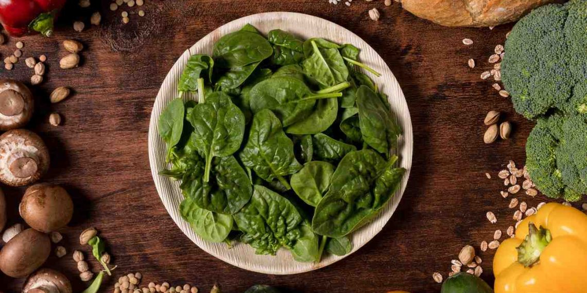 Plate of fresh spinach surrounded by kale and assorted vegetables and bread.