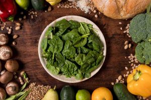 Plate of fresh spinach surrounded by kale and assorted vegetables and bread.