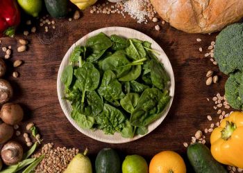 Plate of fresh spinach surrounded by kale and assorted vegetables and bread.