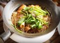 Glass noodles with seafood and fresh herbs in a sizzling pan.