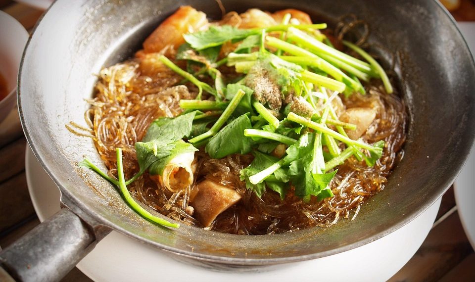 Glass noodles with seafood and fresh herbs in a sizzling pan.