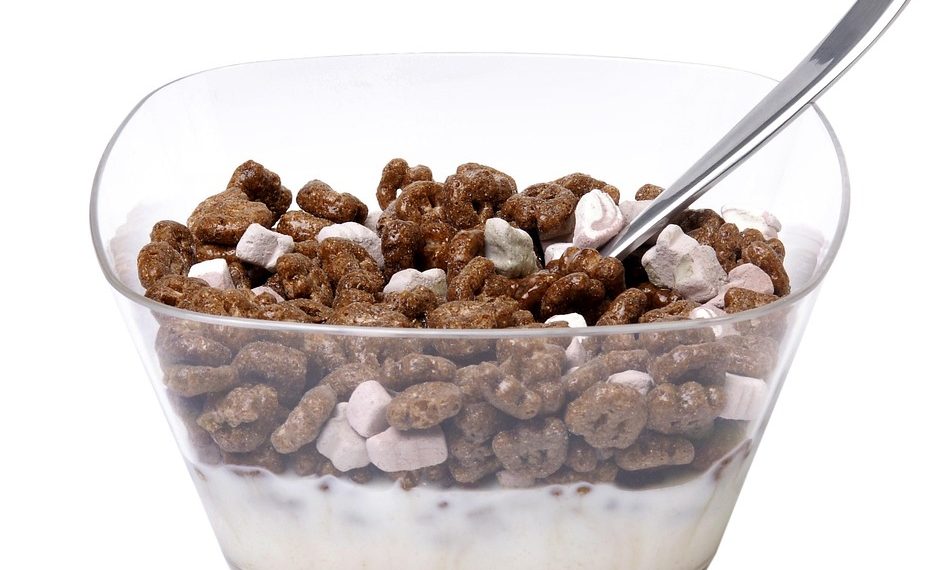 Chocolate cereal and marshmallows in a bowl with milk and spoon.