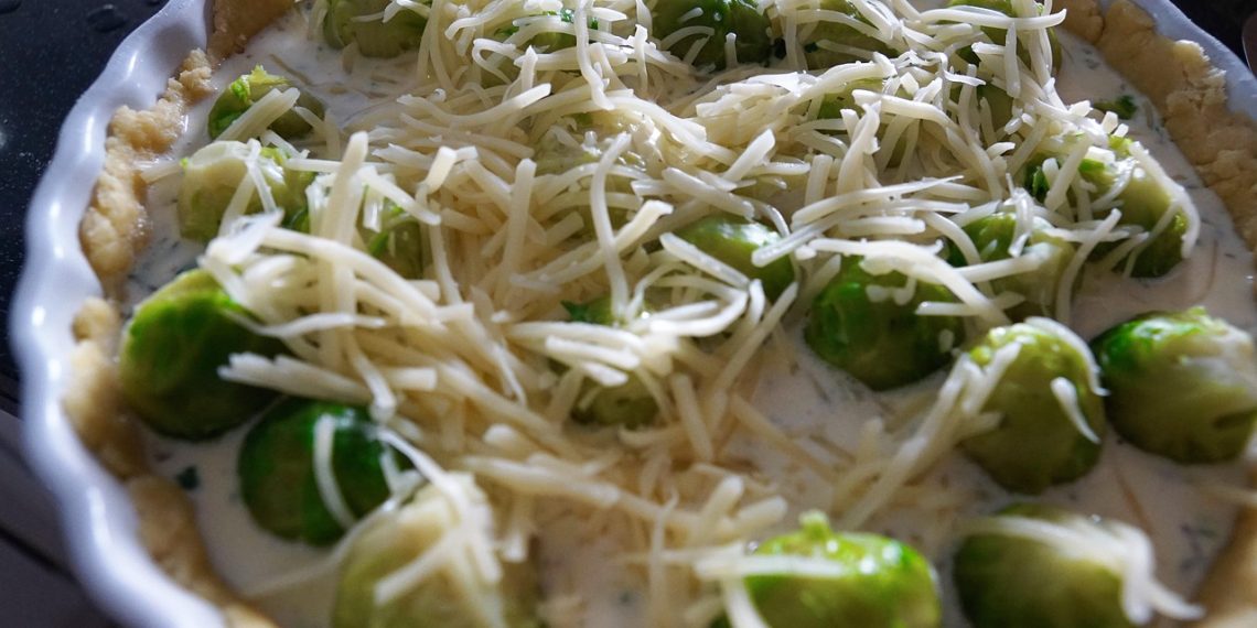 Brussels sprout quiche topped with grated cheese before baking.